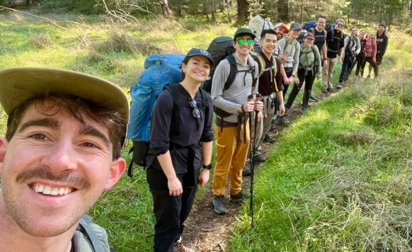 Hex team members on a group hike, taking a trail selfie with a long line of backpackers behind them