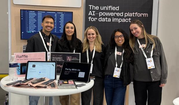 Five Hex team members at a conference booth in front of a banner reading "The unified AI-powered platform for data impact"