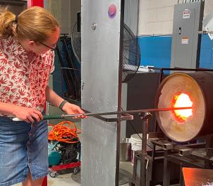 Hex team member trying glassblowing, using a blowpipe at a furnace
