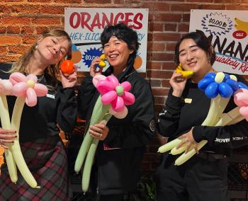 Three Hex team members holding colorful balloon flower animals at an event